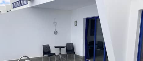 A pool area with a blue pool, two black chairs, a small round table, and a blue-framed sliding door.