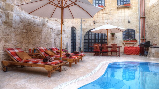 A poolside area with lounge chairs and umbrellas, stone walls, and a clear blue pool. - Id-Dwejra  House  of Character with Privite Pool,  swim Jet and Jaccuzzi (Zejtun)