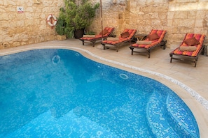 Une piscine avec des chaises longues et un mur en pierre.