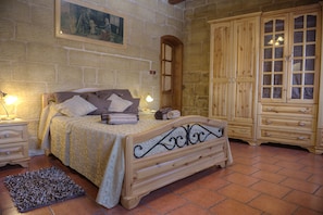 Une chambre avec un mur en pierre, un lit doté d’une tête de lit, une armoire en bois et un tableau accroché au mur.