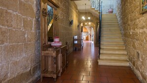 A stone-walled hallway with a wooden bench, a staircase, and a view into a room with a kitchen. - Id-Dwejra  House  of Character with Privite Pool,  swim Jet and Jaccuzzi (Zejtun)