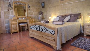A bedroom with a stone wall, a wooden bed, a nightstand, a dresser, a mirror, and a painting. - Id-Dwejra  House  of Character with Privite Pool,  swim Jet and Jaccuzzi (Zejtun)