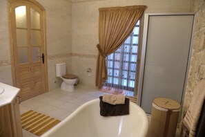 Une salle de bain avec une baignoire, des toilettes et une fenêtre avec des rideaux.