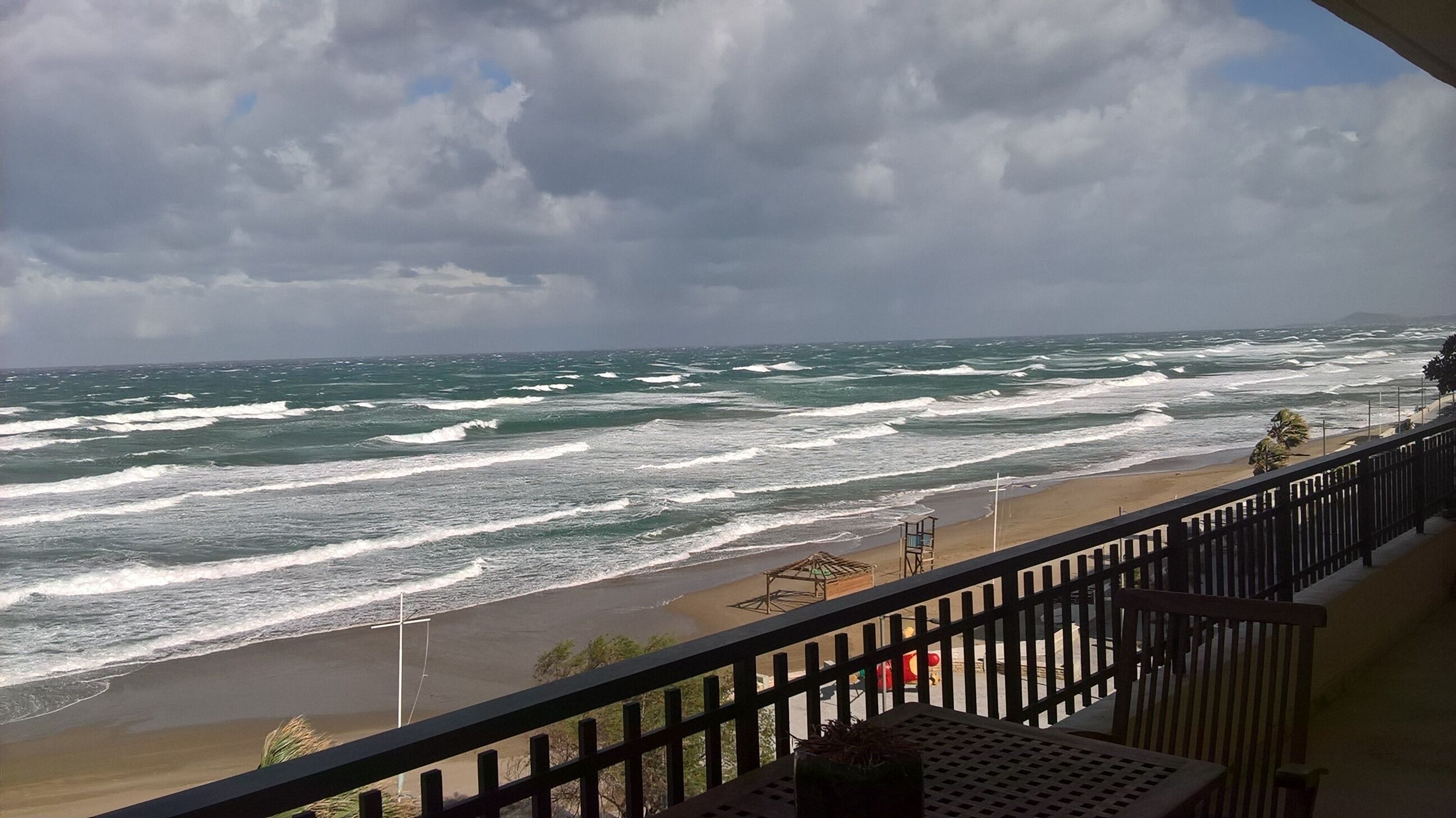 A balcony with a view of the ocean, a beach, and a lifeguard tower.