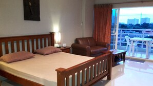 A hotel room with a bed, a chair, a small table, and a view of the city through the window.