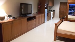 A bedroom with a wooden bed, a TV, a laptop, and a washing machine in the background.