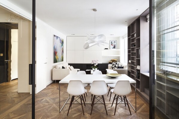 A modern dining area with a white table, four chairs, and a unique pendant light.