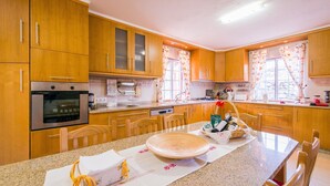 Eine Küche mit Holzausstattung, einem Edelstahlbackofen, einem Esstisch mit Stühlen und einem Fenster mit Vorhängen.