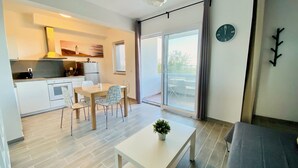 Een moderne keuken met witte kasten, een eethoek met tafel en stoelen, en een balkon met uitzicht.