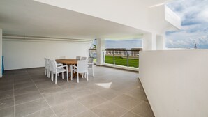 A spacious balcony with a dining area, a view of a green field, and a clear sky. - Spectacular Sea Front Villa - The Waterfront (Marsaskala)