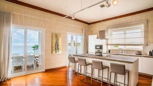 A modern kitchen with a large island, bar stools, and a view of the ocean through sliding glass doors. - Spectacular Sea Front Villa - The Waterfront (Marsaskala)