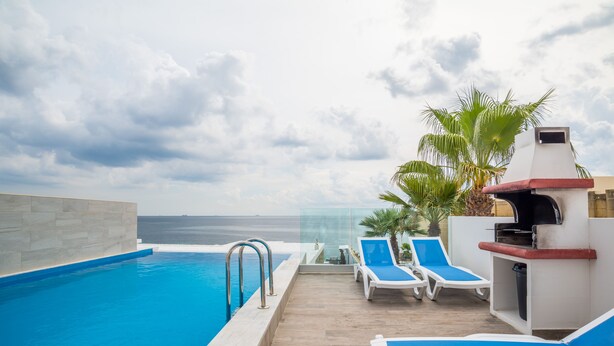 A pool area with a view of the ocean, lounge chairs, and a barbecue grill. - Spectacular Sea Front Villa - The Waterfront (Marsaskala)