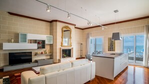 A modern kitchen with a built-in island, a white sofa, and a flat-screen TV. - Spectacular Sea Front Villa - The Waterfront (Marsaskala)