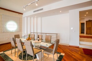 A modern dining area with a glass table and metal chairs, a wooden floor, and a red rug.