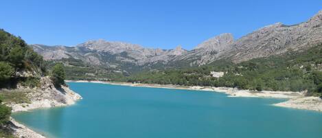 A coastal landscape with a turquoise lake, rocky mountains, and sparse vegetation.
