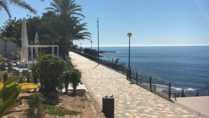Un paseo marítimo con sendero de baldosas, bancos y barandilla con vistas al mar.