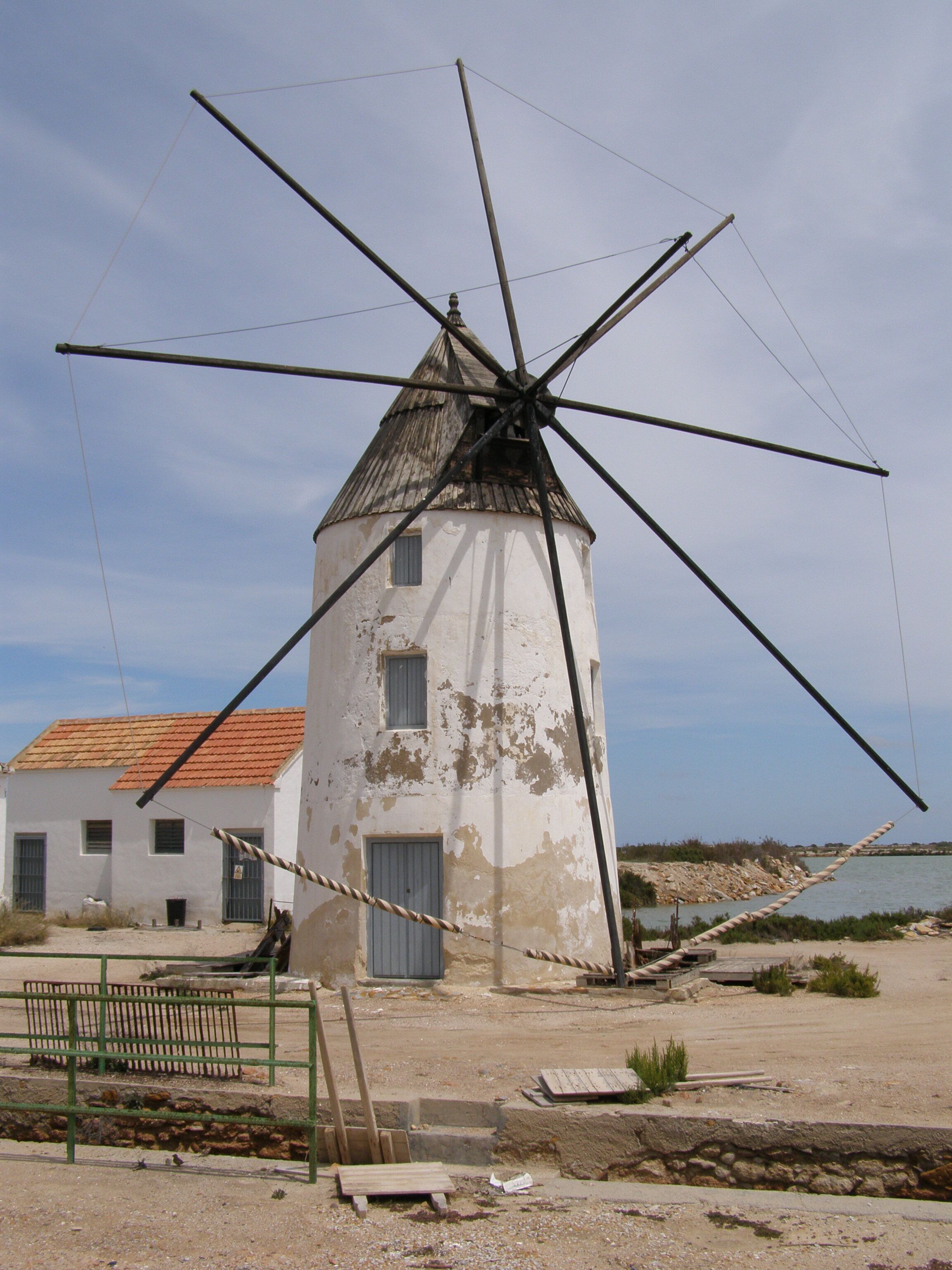 A windmill with a white facade and a red-tiled roof, situated next to a building with a white exterior and a red roof.