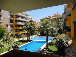 Une cour d’hôtel avec une piscine, des palmiers et des immeubles à plusieurs étages.