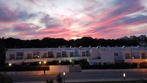 Una hilera de edificios modernos de una sola planta con techos planos y antenas parabólicas, posiblemente viviendas o unidades de un pequeño hotel, bajo un cielo crepuscular con nubes rosadas y moradas.