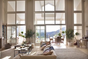 A spacious living room with a large window, a sofa, a coffee table, and a dining area with chairs and a table. - Luxury Country Estate, with Outdoor Swimming-pool & Heated Indoor Pool. (Gaucin)