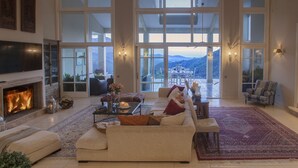 Un salon spacieux doté d’une cheminée, d’un grand canapé, d’un coin repas avec des chaises et offrant une vue sur les montagnes grâce à de grandes fenêtres.