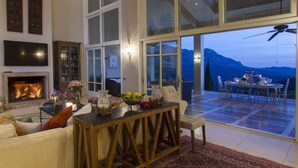 Un salon chaleureux avec une cheminée, un coin repas offrant une vue sur les montagnes et une grande porte vitrée donnant sur l’extérieur.