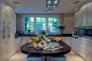 A kitchen with a central island, white cabinets, and a large window with greenery outside. - Luxury Country Estate, with Outdoor Swimming-pool & Heated Indoor Pool. (Gaucin)