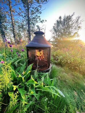 A metal lantern with a fire burning inside, surrounded by lush greenery and flowering plants.