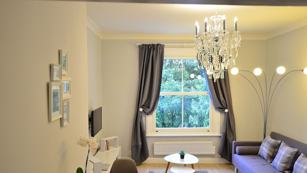 Ein modernes Wohnzimmer mit Essbereich, einer Kristallleuchtre und Blick auf Bäume durch das Fenster.