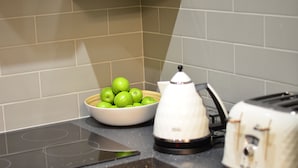 Eine Küchenarbeitsfläche mit einer Schüssel grüner Äpfel, einem weißen Wasserkocher und einem weißen Toaster.