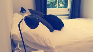Ein ordentlich bezogenes Bett mit weißen Leinen, einer schwarzen Lampe und einem Fenster mit Vorhängen.