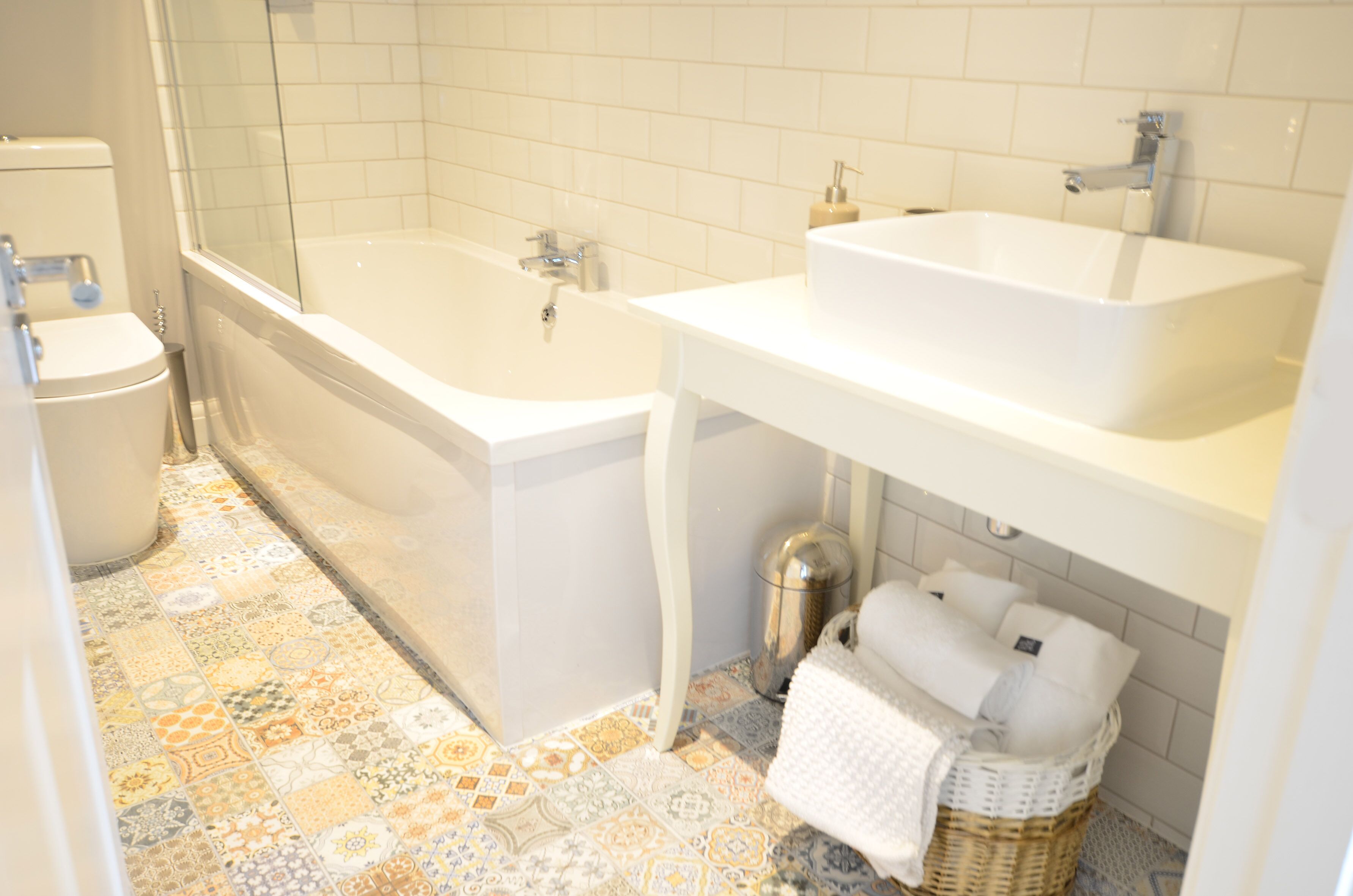 A bathroom with a bathtub, two sinks, a toilet, and a patterned floor.