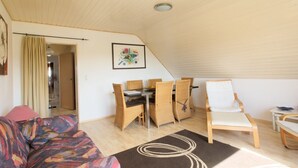 A cozy living room with a sofa, a dining table with chairs, and a chair with a cushion.