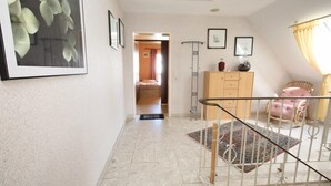 A hallway with a tiled floor, a wooden cabinet, a framed picture, and a chair.
