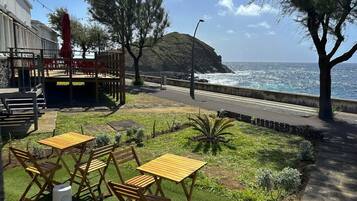 A patio area with outdoor seating, a view of the ocean, and a grassy landscape with trees.