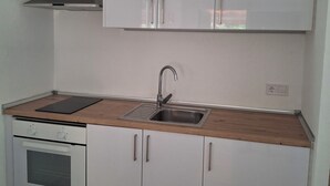 Uma cozinha compacta com armários brancos, uma pia de aço inoxidável e um forno embutido.