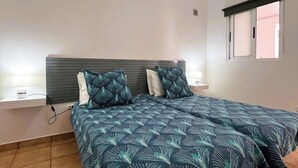 Une chambre à coucher comprenant un lit, une table de chevet, une fenêtre avec un store et un luminaire au plafond.
