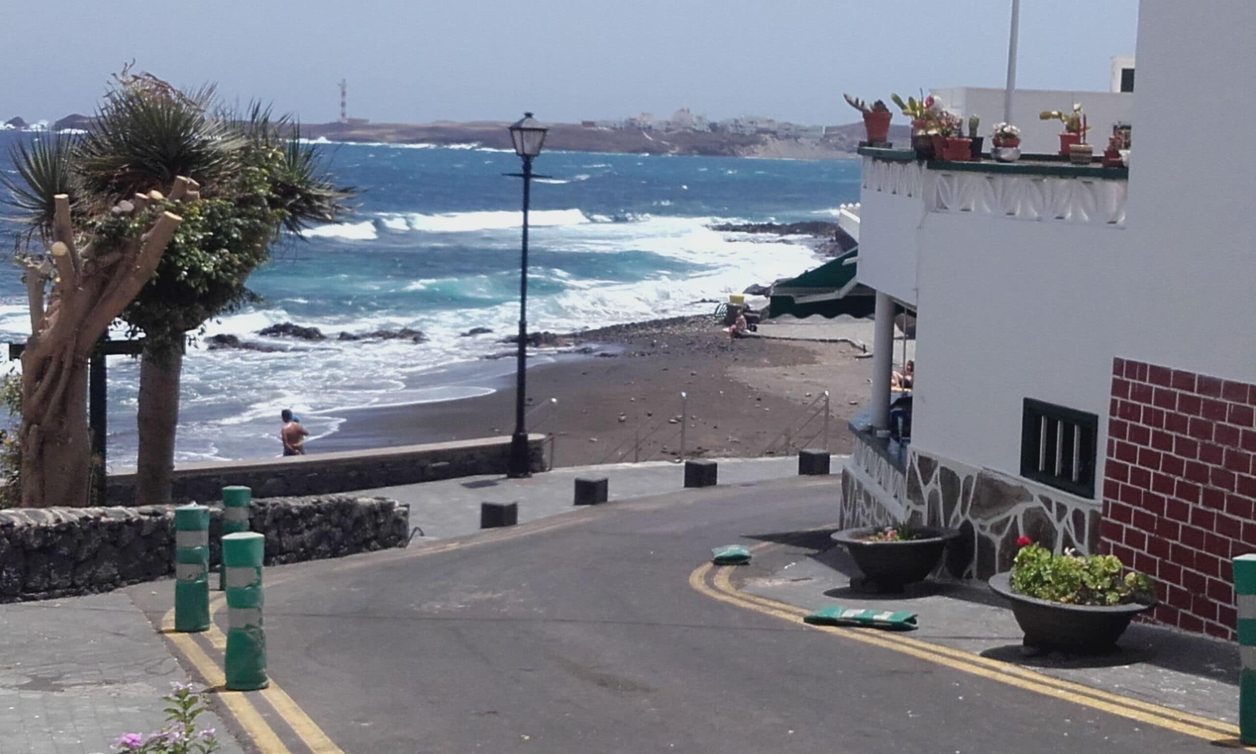 Une route côtière offrant une vue sur la mer, un palmier et un bâtiment doté d’un balcon.