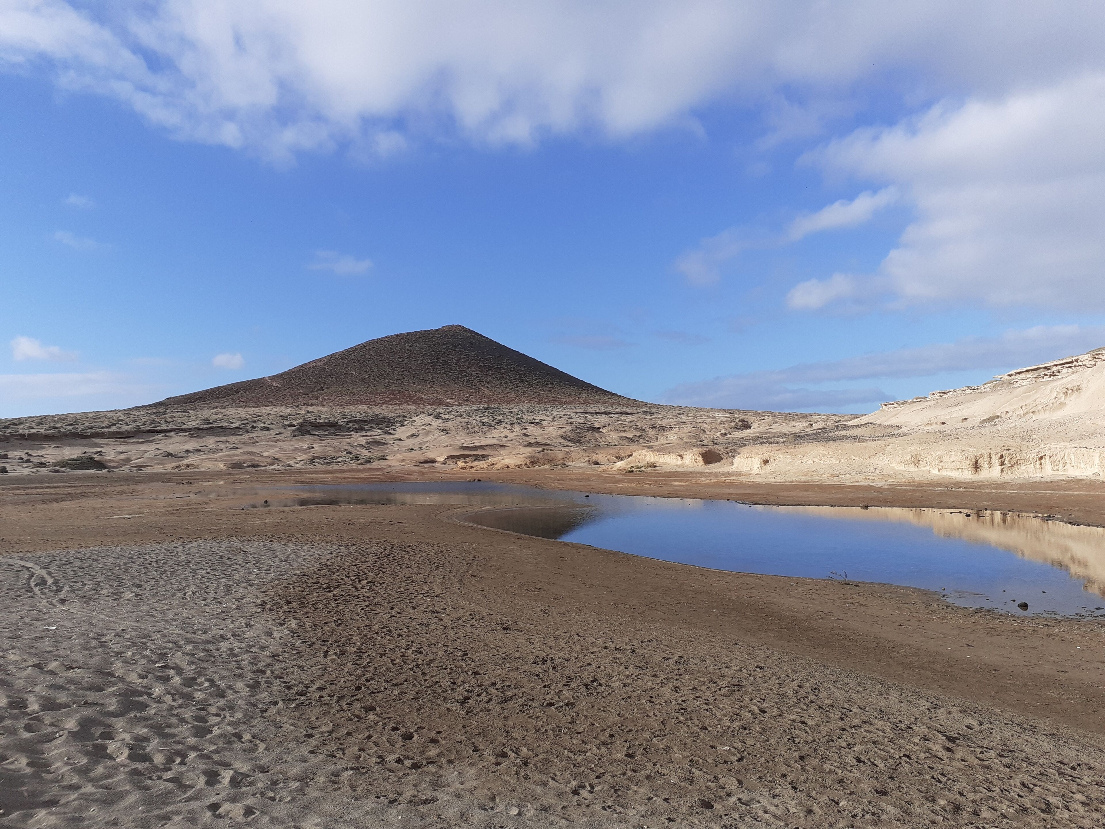 A desert landscape with a large hill and a small pond.