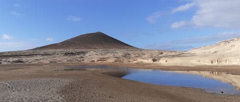 A desert landscape with a large hill and a small pond.
