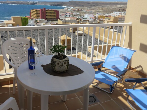 A balcony with a table, chairs, a decorative owl, a bottle, and a glass.