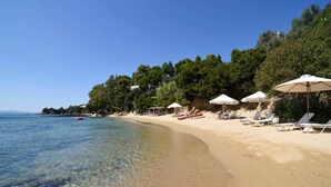 Une plage avec une eau cristalline, des parasols blancs et des chaises longues.