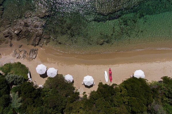 Vista aérea de una playa con agua cristalina, un kayak rojo y varios sombrillas blancas.