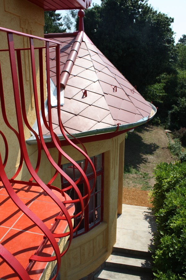A corner of a building with a red metal railing and a tiled roof.