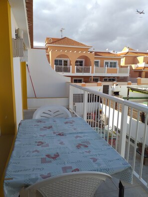 A balcony with a table covered in a patterned tablecloth, a white chair, and a view of neighboring buildings with a tiled roof. - Sun & Sol apartment in Caleta de Fuste (Castillo Caleta de Fuste)