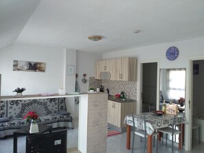 A modern living room with a sofa, a dining table with chairs, a kitchen area with wooden cabinets, and a clock on the wall. - Sun & Sol apartment in Caleta de Fuste (Castillo Caleta de Fuste)