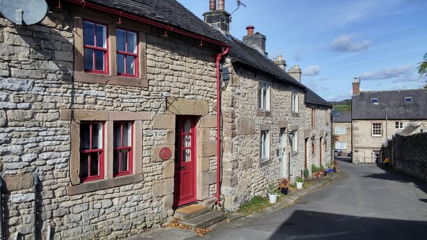 Un bâtiment en pierre avec une porte et des fenêtres rouges, une antenne parabolique bien visible et un ciel dégagé.