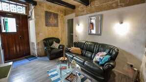 Una sala de estar con un sofá de cuero, una mesa de centro de vidrio y una alfombra. Hay una puerta con un letrero de 'EXIT' y un espejo en la pared.