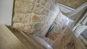 Interior con paredes de piedra, una escalera de madera y una escultura decorativa de metal.