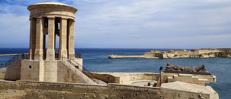 Une fortification côtière dotée d’une tour centrale, d’un escalier menant à la tour et d’une statue située à droite.